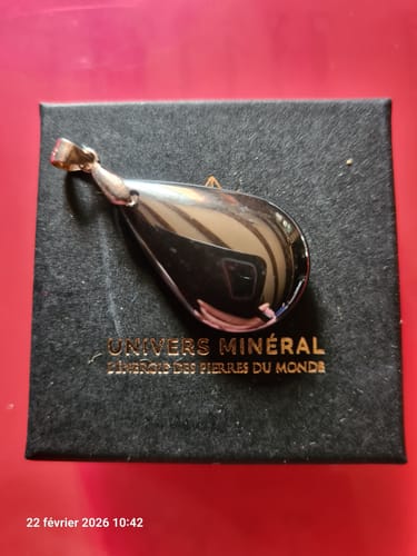 Le pendentif hématite d'un client, une pierre brillante en forme de goutte, posé sur sa boîte d'origine.