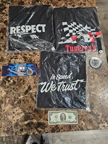 Customer's contents from the Mystery Cash Box, including three black graphic t-shirts, two stickers, and a two-dollar bill.