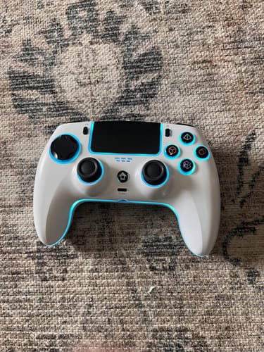 Reviewer's white Wireless Game Controller illuminated with vibrant blue RGB lighting on a patterned rug.