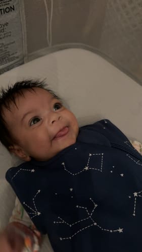 Customer's happy baby wearing the dark blue Night Sky™ baby sleeping bag in a crib.