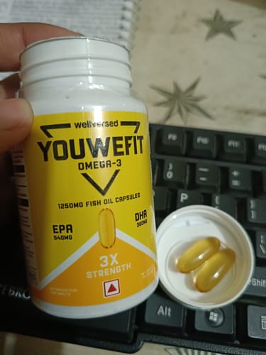 Customer holding the YouWeFit Omega-3 Fish Oil bottle with two golden capsules displayed in the open lid.