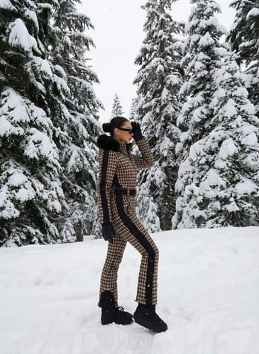 Reviewer standing in a snowy forest wearing the chic houndstooth one-piece ski suit.