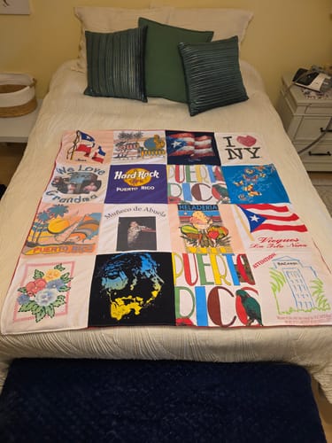 Reviewer's custom Premium T-Shirt Quilt made from their mother's shirts, spread across a bed in a brightly lit bedroom.