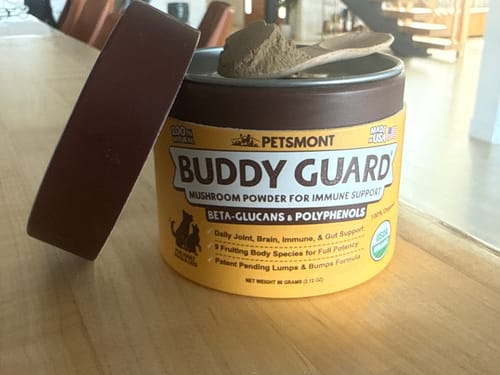 Reviewer's open yellow container of Petsmont Buddy Guard powder with a scoop of the supplement resting on top.
