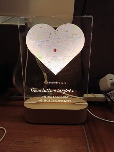 Das personalisierte Nachtlicht eines Kunden, beleuchtet, zeigt eine herzförmige Karte und eine Gravur auf dem Holzsockel.