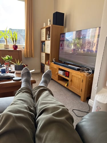 Customer relaxing on a couch while wearing a comfortable pair of grey Crew Socks.
