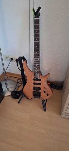 Rezensent zeigt die Donner HLX-500 Headless E-Gitarre auf einem Ständer in einem Raum.