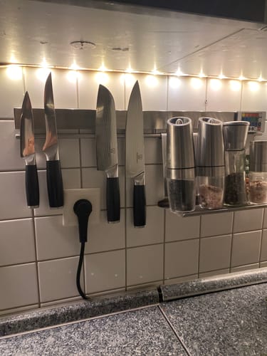 Ein Kunde zeigt vier OKAMI Messer mit schwarzen Griffen, die an einer Magnetleiste in einer modernen Küche hängen.