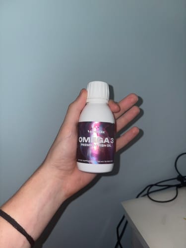 Customer holding a white bottle of Omega 3 Premium Fish Oil in their hand against a blue wall.