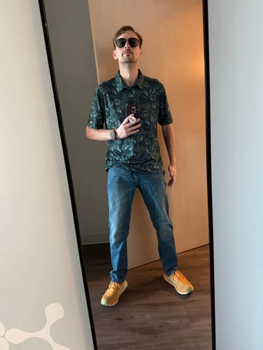 Reviewer showing the fit of the dark green Jurassic Park "Clever Girl" polo in a mirror selfie.