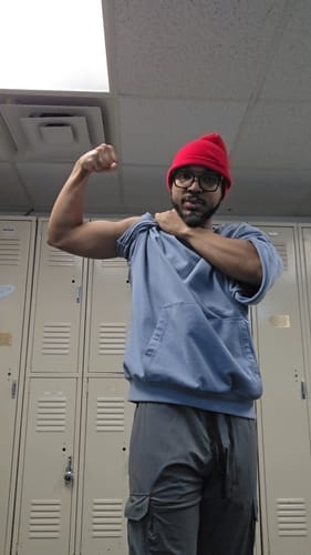 Reviewer in a locker room flexing, pulling up the sleeve of their oversized blue Megàlo 3/5 Sleeve Crewneck.