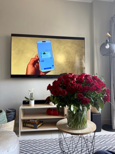 Customer's Golden Majesty red roses displayed in a large glass vase in a living room.