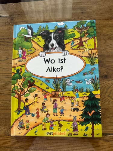 Kunde zeigt das personalisierte Wimmelbuch „Wo ist Aiko?“. Das bunte Cover zeigt einen Border Collie in einem Park.