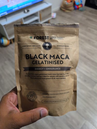 Reviewer holding the brown paper pouch of Forest Super Foods Gelatinized Black Maca Powder.