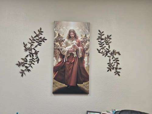 Reviewer's 'Jesus Protects The Lamb From Wolves' wall art hanging on a white office wall between two decorative sconces.