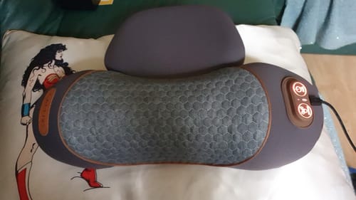 Customer's gray Original Callixe Thera Pillow with its textured fabric, plugged in and resting on a couch pillow.