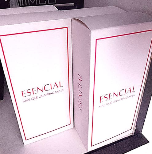El cliente muestra dos cajas de su perfume M024. Son cajas blancas con el logo de 'Esencial' en rojo.