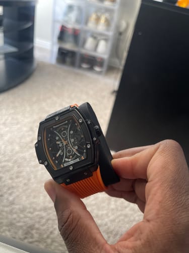 A reviewer holds their Lucky Fours® Summit watch, showing its black case and bright orange band.