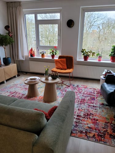 De oranje en rode Fauteuil Ally van een klant in een woonkamer met een kleurrijk vloerkleed.