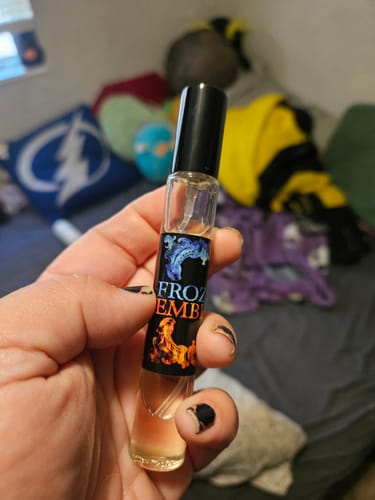 Customer holding a small rollerball bottle of Frozen Embers perfume, showing the label design.