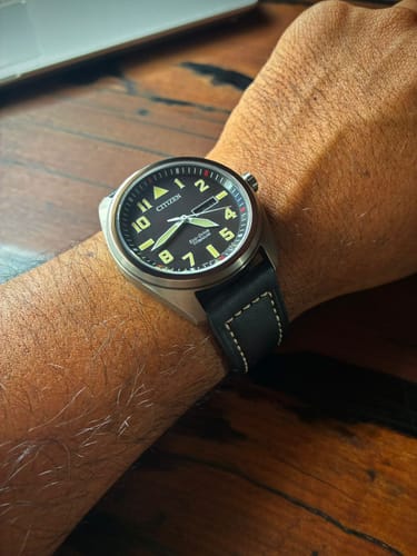 Un cliente muestra su reloj Citizen Eco-Drive en la muñeca, con la esfera negra y la correa de cuero con costuras.