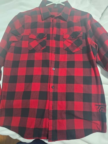 Customer's red and black PENDANT FLANNEL shirt laid out flat, showing the plaid pattern and embroidered logo on the hem.