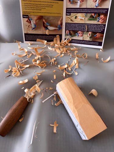 Customer's wood carving project from the Craft DIY Subscription Box, with a whittling knife and wood shavings on a table.