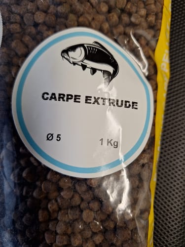 Een recensent toont een detailopname van de 1 kg verpakking Carpe Extrudee-pellets.
