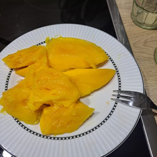 Kunde zeigt sehr reife, saftige Stücke der Bio Keitt Mango auf einem Teller.