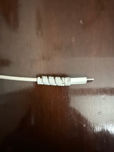Close-up of a customer's white cable protector wrapped around the end of a charging cable on a wooden surface.