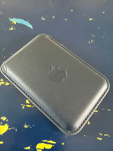 Customer's deep blue Signature Leather Magsafe Wallet for iPhone resting on a dark, paint-splattered surface.