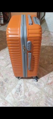 Cliente muestra su sólida maleta de viaje Monarca naranja, de pie y vista desde un costado.