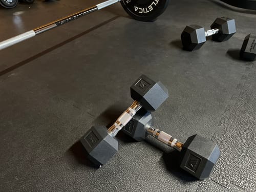 Ein Kunde zeigt seine Sammlung von Hexagon Hanteln, die auf einer schwarzen Bodenmatte liegen.