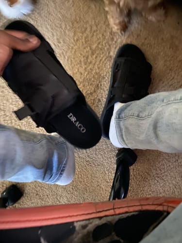 Reviewer's view of their black slides, wearing one with jeans and holding the other to show the brand name.