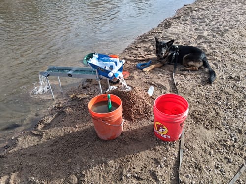 Customer's Highbanker Sluice Box set up and running on a riverbank next to their dog and buckets.