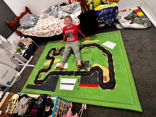 Customer's child sitting on a soft green Relax Mat with a racetrack design in a messy bedroom.
