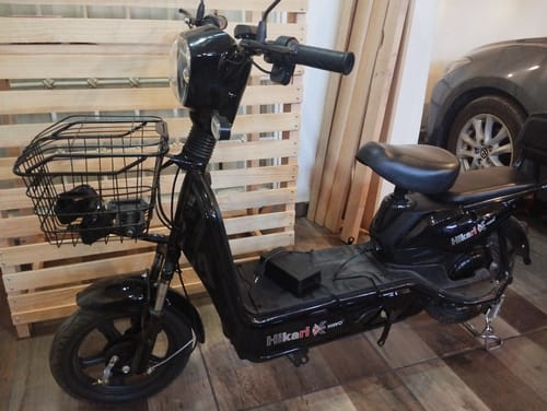 La Bicicleta Eléctrica Negra Kiwo de un cliente, estacionada en interiores con una canasta frontal.