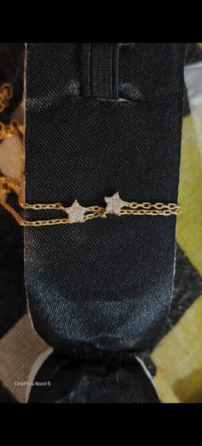 Reviewer's Golden Star Constellation Anklet, with its double gold chain and two zircon stars, laid across a black pouch.