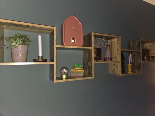 Recensent toont de roze Karlsson 'Modern Doggy' wandklok op een houten wandplank.