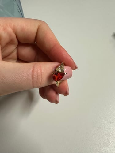 Customer's hand holding the Leesha Birthstone Ring, which features a red and a clear pear-shaped stone on a gold band.