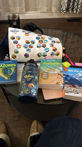 Customer's blue World Explorer Bottle and sticker sheet on a coffee table with travel guidebooks for planning.