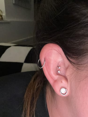 Customer's ear showing two Solitaire flatback Silver studs in a double flat piercing, alongside other earrings.