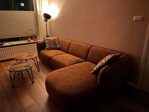 Klant toont de terra-kleurige by fonQ Soft hoekbank in een sfeervol verlichte woonkamer.
