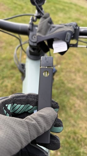 Customer's gloved hand holding the dark ROLLZ THCA Vape outdoors with a bicycle in the background.