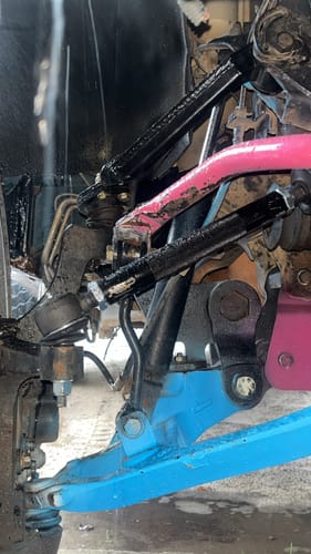 Close-up of customer's black heavy-duty tie rods installed on a truck's custom blue and pink front suspension.