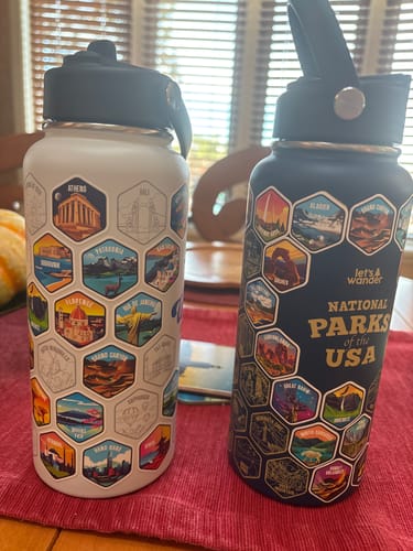 Customer's white World Explorer and dark National Parks Lets Wander™ water bottles with travel stickers applied.