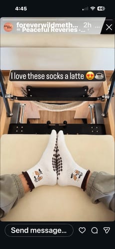 Reviewer's feet in white Pilates & Lattes socks with grippy soles, resting in front of a Pilates machine.