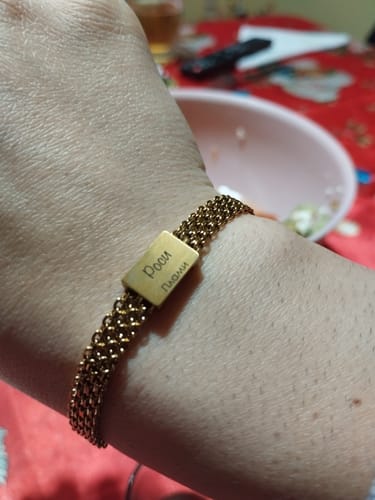 Close-up of a reviewer's wrist wearing the woven, gold-colored Zara bracelet with a personalized engraved plate.