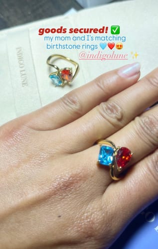 Customer wearing a Navae Birthstone Ring with blue and red stones, with a matching ring shown in the background.