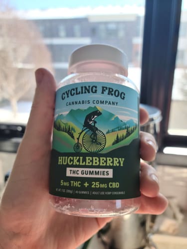 Reviewer holding an almost-empty clear bottle of Huckleberry THC Gummies in their hand.